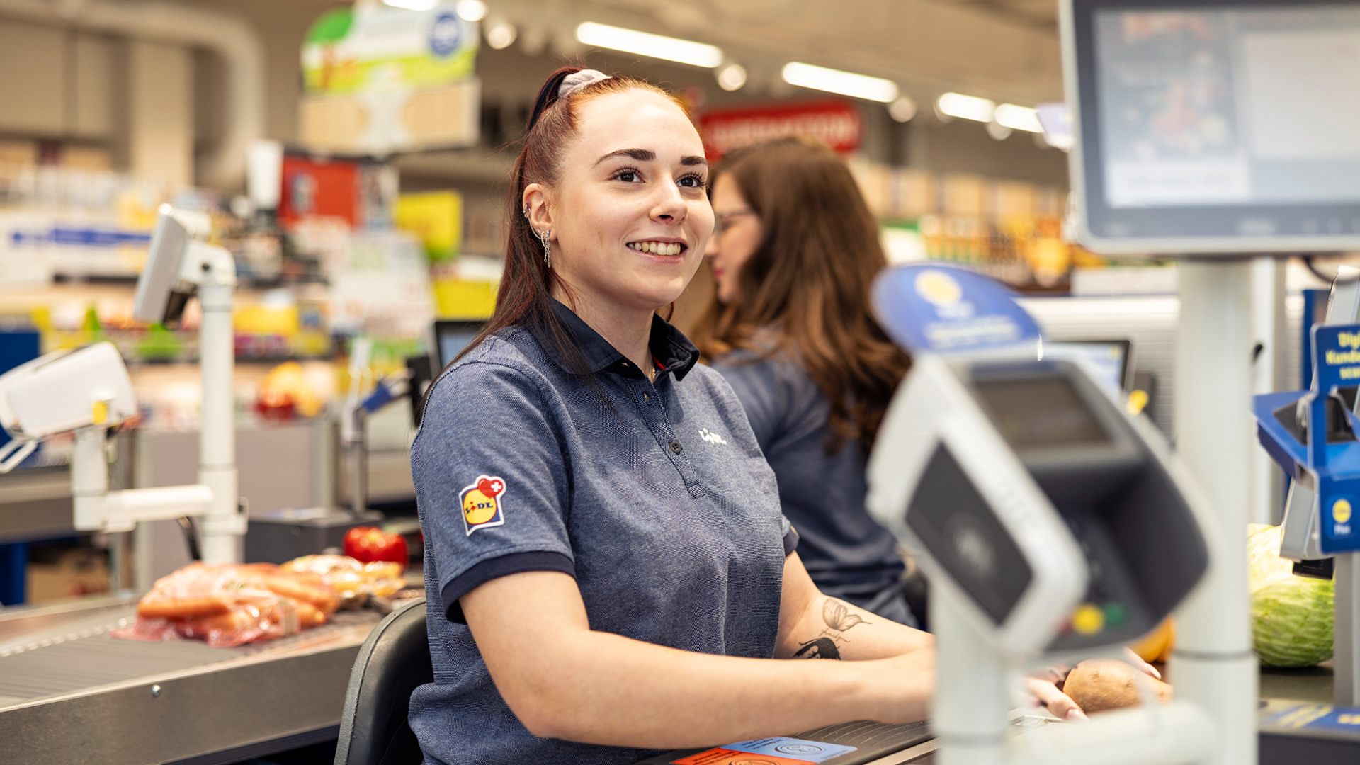 Un employé de Lidl, tout sourire, en train de scanner des produits d'épicerie à une caisse.