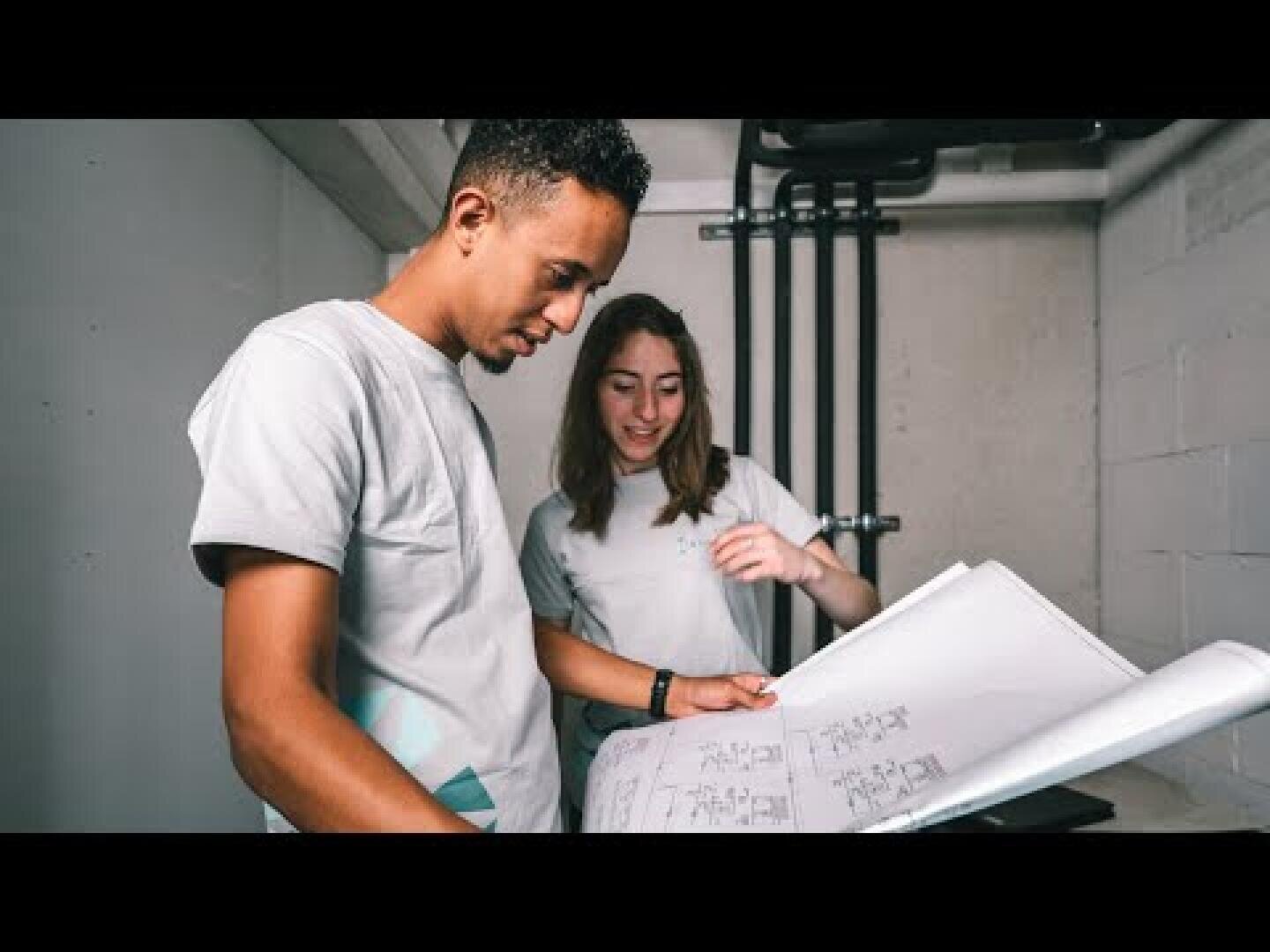 Deux personnes vêtues de chemises décontractées examinent une série de plans d'architecture.