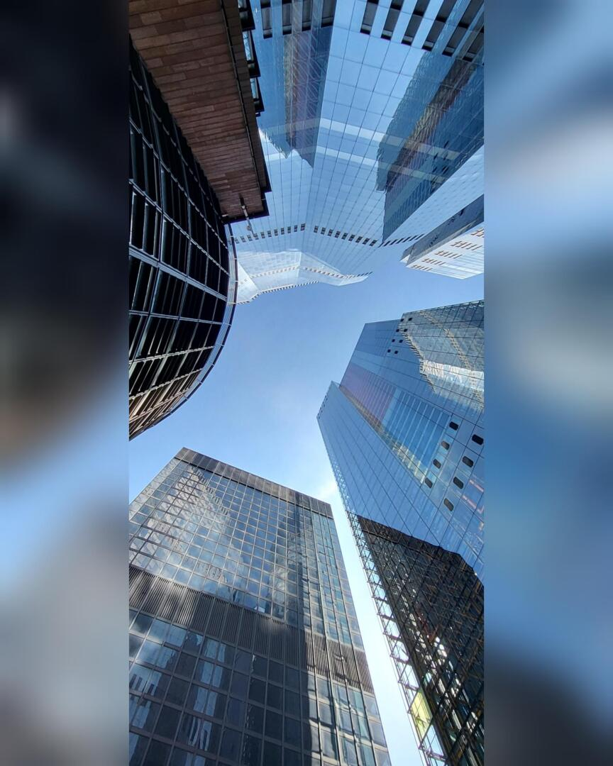 Vue spectaculaire vers le haut de plusieurs gratte-ciel modernes en verre avec des surfaces réfléchissantes, convergeant vers un ciel bleu vif, créant une impression de hauteur et d'architecture urbaine.