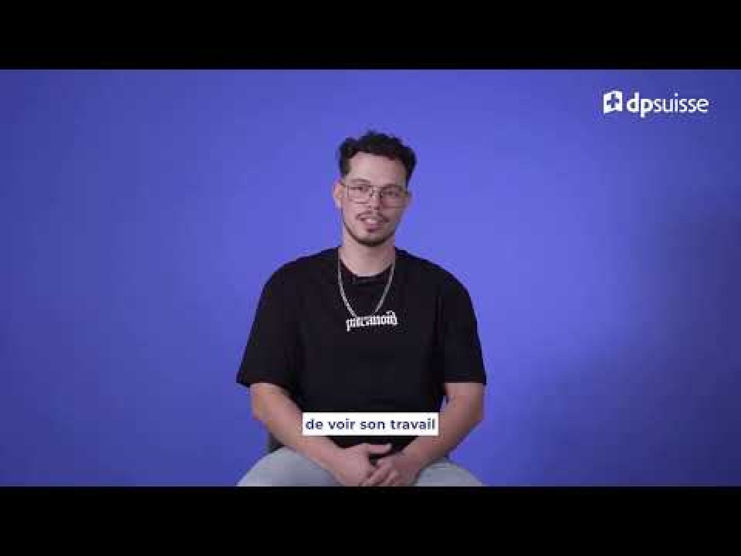 Un homme portant des lunettes et un t-shirt noir est assis sur un tabouret sur fond bleu uni. Le logo dpsuisse apparaît en haut à droite, et le texte français en bas indique « de voir son travail ».