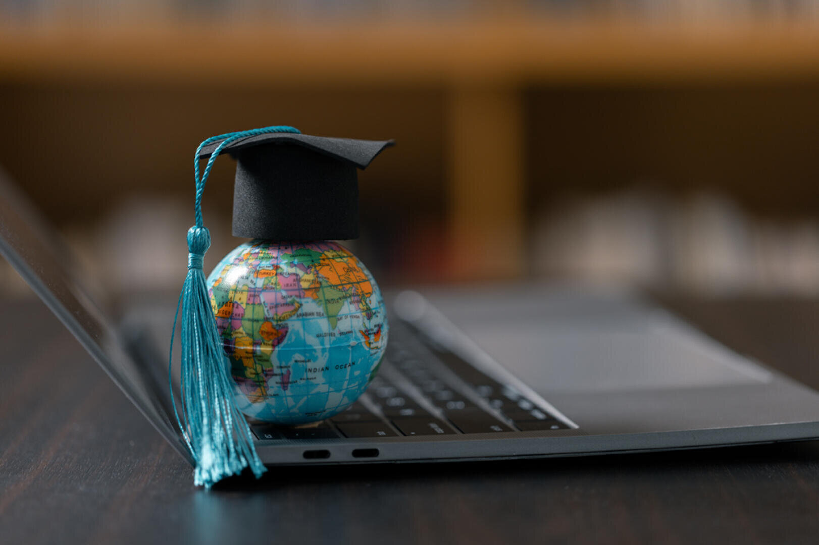 Un petit globe coiffé d'un bonnet de fin d'études avec un pompon bleu est posé sur le clavier d'un ordinateur portable ouvert, symbolisant l'éducation mondiale en ligne ou les études internationales.