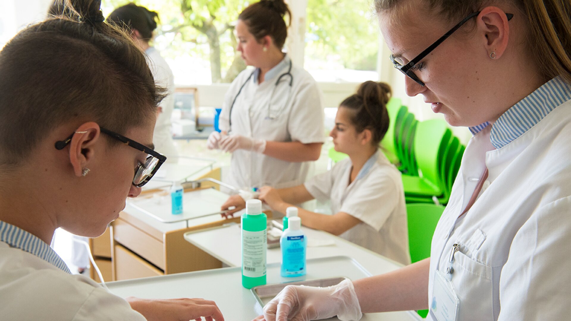Quatre professionnels de la santé en uniforme blanc et gants sont réunis autour d'une table dans une pièce lumineuse, effectuant des procédures médicales avec des flacons de désinfectant et du matériel médical visibles sur la table.