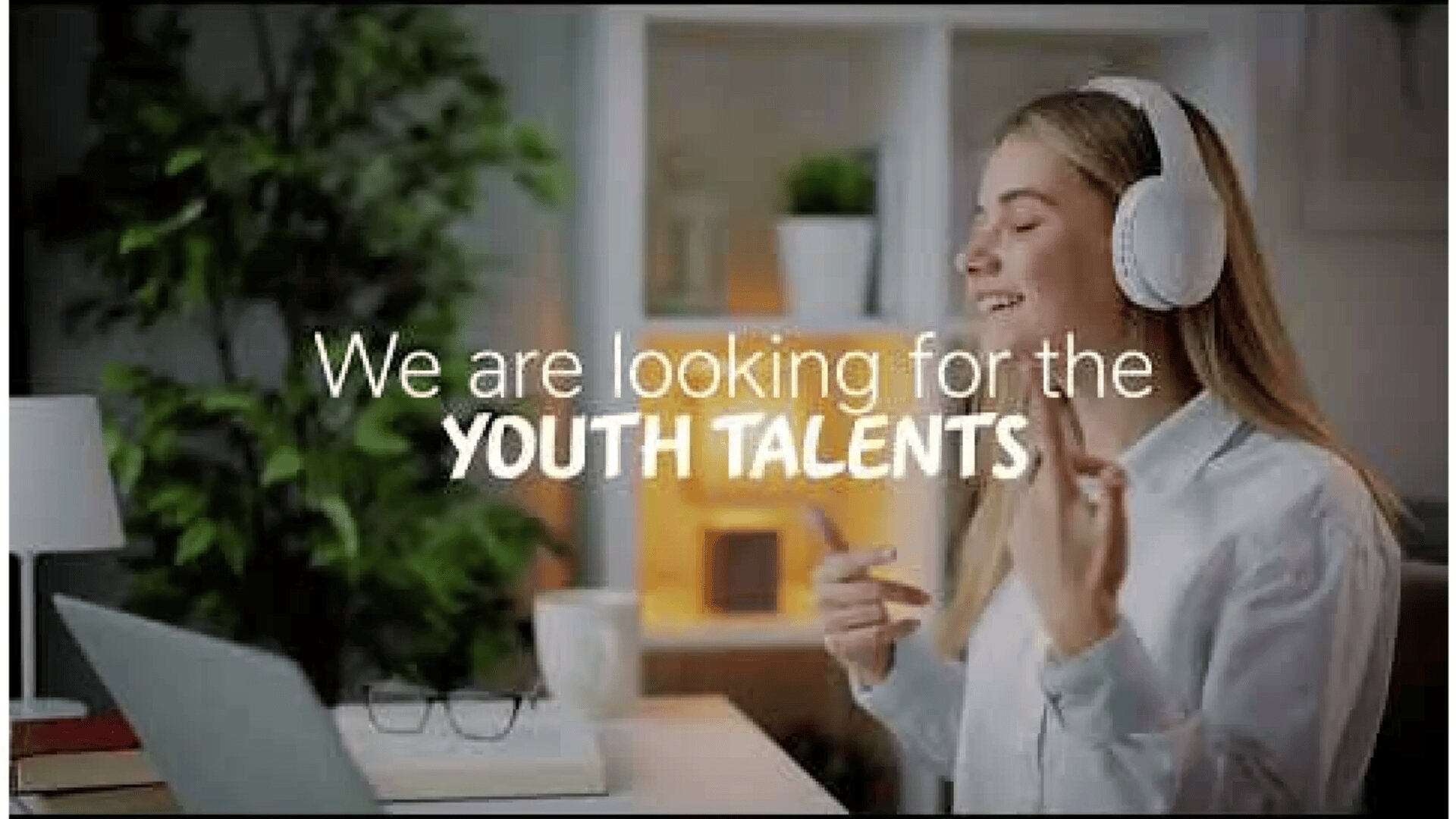 Une jeune femme portant des écouteurs sourit et fait des gestes en écoutant de la musique. Le texte en incrustation indique : "Nous recherchons les TALENTS DE LA JEUNESSE". Elle est assise dans une pièce bien éclairée avec des étagères et une plante en arrière-plan.