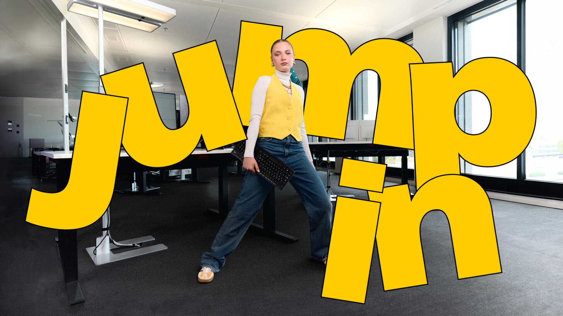 Une personne se tient debout, confiante, dans un bureau, vêtue d'un gilet jaune et d'un jean ample, tenant un clavier. Un grand texte jaune indiquant "jump in" est superposé, masquant une partie de l'arrière-plan du bureau.