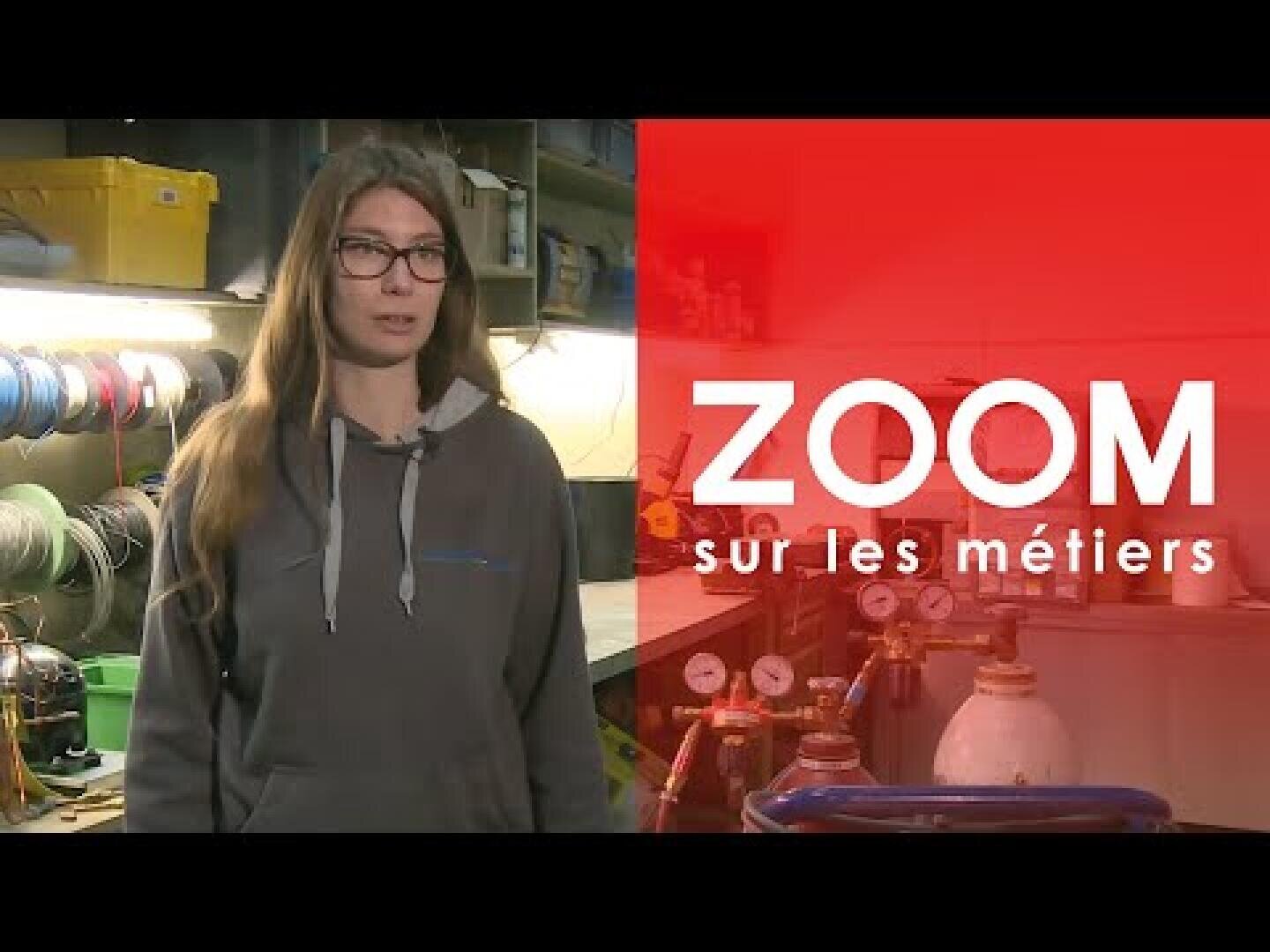Une jeune femme vêtue d'un sweat à capuche gris se tient debout dans un atelier, sur lequel apparaît le texte ZOOM sur les métiers sur fond rouge.