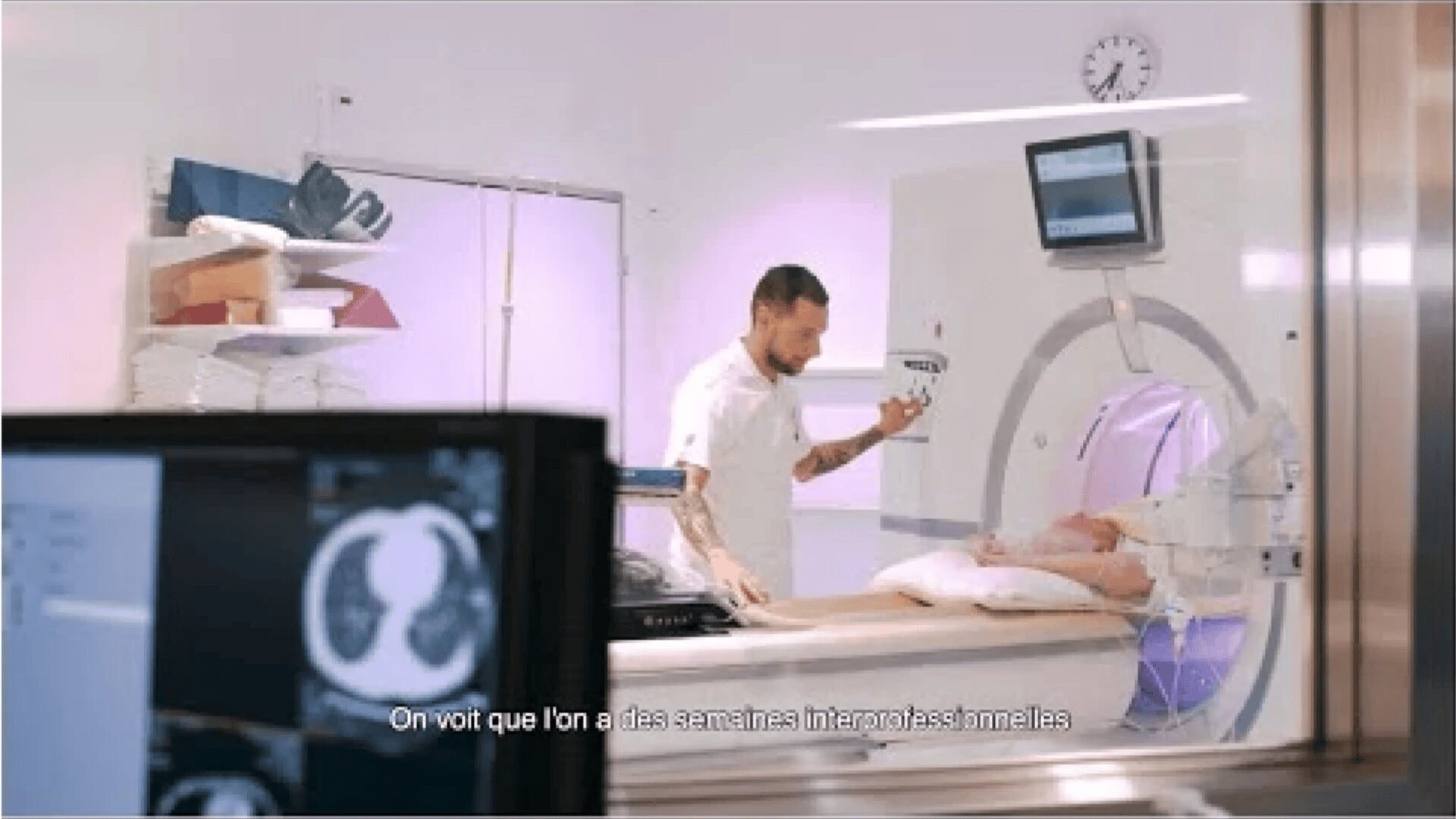 Un technicien médical prépare un patient pour un scanner dans une chambre d'hôpital. Des images médicales sont visibles sur un écran au premier plan. Des sous-titres en français sont affichés en bas de l'image.
