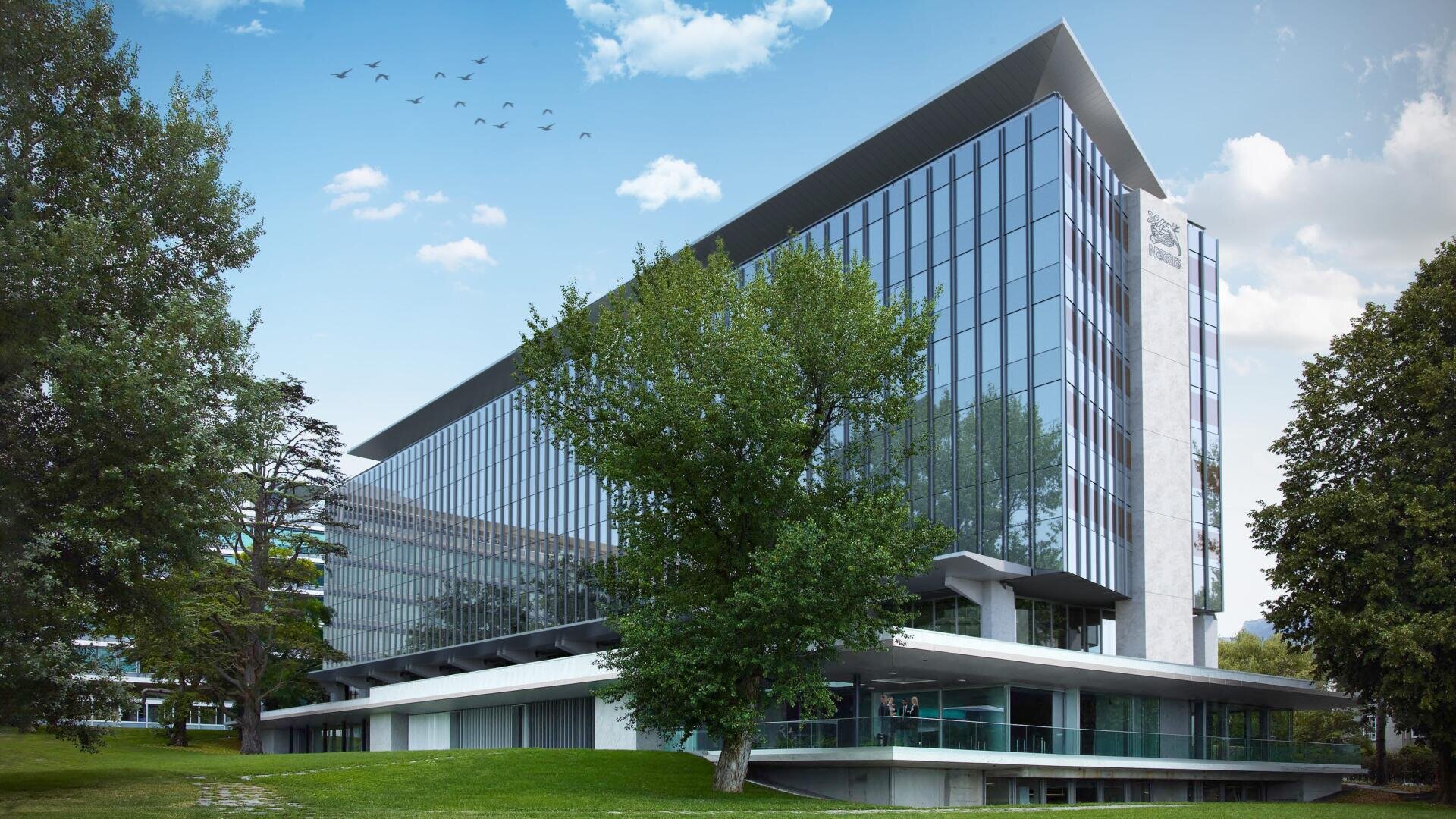 Un immeuble de bureaux moderne en verre entouré d'arbres verts et d'herbe, avec des oiseaux volant dans le ciel bleu. La scène est lumineuse et paisible.