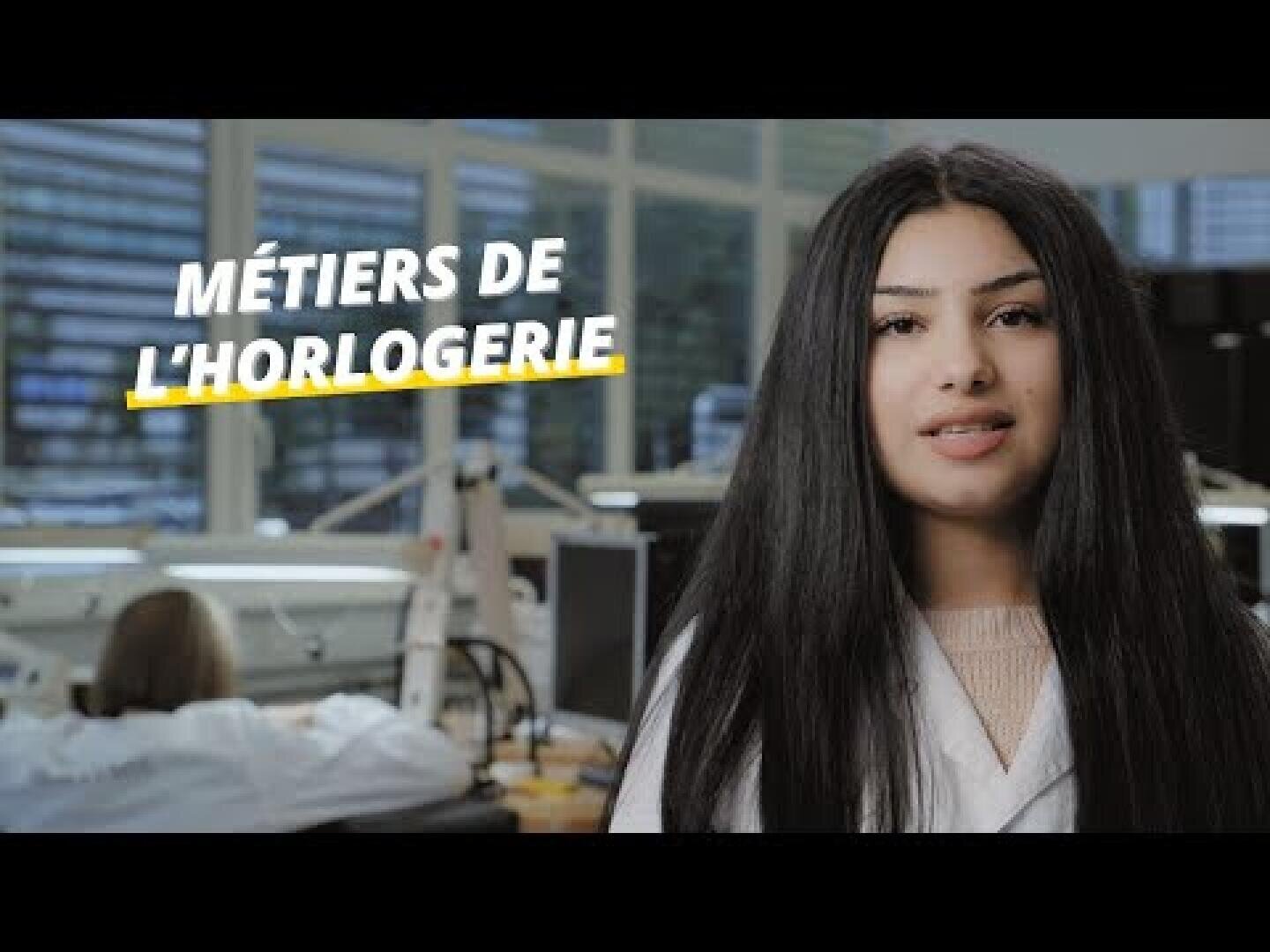 Une femme aux longs cheveux noirs, vêtue d'une blouse blanche, se tient dans un atelier lumineux ; le texte « Métiers de l'horlogerie » apparaît sur l'image. Une autre personne travaille à un bureau en arrière-plan.