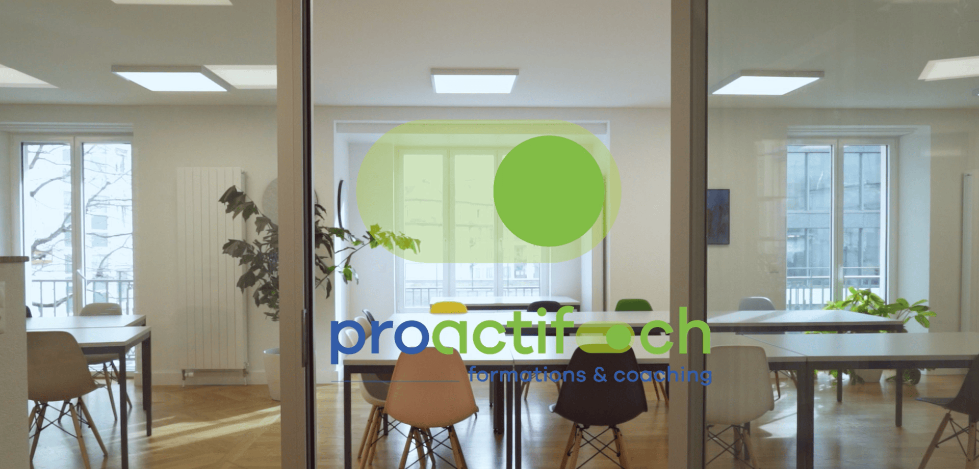Bureau moderne avec des murs en verre montrant le logo "proactif coaching formations & coaching", avec une bulle verte, et des tables de réunion avec des chaises à l'intérieur d'une pièce lumineuse.