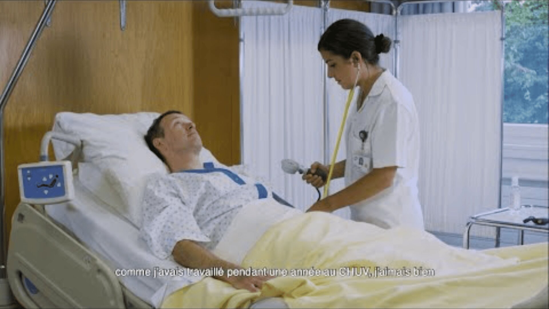 Un médecin en blouse blanche utilise un stéthoscope pour examiner un homme allongé dans un lit d'hôpital. Le patient porte une blouse médicale et du matériel hospitalier est visible dans la pièce. Le texte français est superposé en bas.